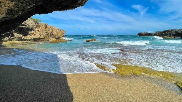 A coastal scene with clear skies, a rocky shoreline, and waves crashing onto the beach.