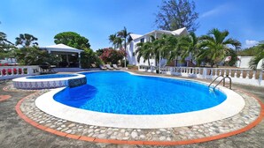 A swimming pool with a stone border, lounge chairs, and a covered area with a grill.