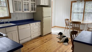 Une cuisine avec des meubles blancs, un réfrigérateur, un évier et un coin repas avec des chaises.