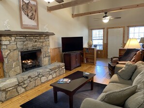 A cozy living room with a stone fireplace, a flat-screen TV, a leather sofa, and a wooden coffee table.