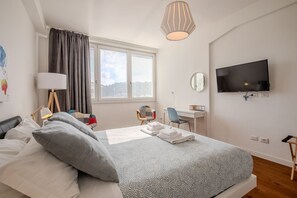 A modern bedroom with a bed, a desk, a chair, a TV, and a window with curtains.