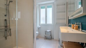 A modern bathroom with a glass shower enclosure, a white sink with wooden accents, and a toilet with a small step stool. - Elisa apartment Sistine Chapel (Roma)