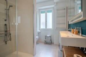 A modern bathroom with a glass shower enclosure, a white sink with wooden accents, and a toilet with a small step stool.