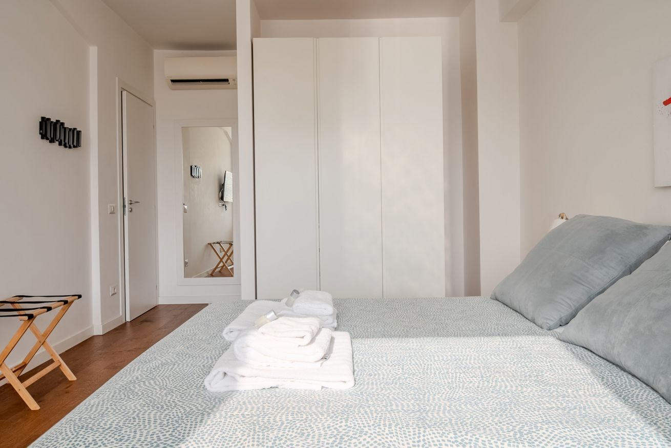 A bedroom with a bed, a folded towel on the floor, a wooden drying rack, and a white wardrobe.