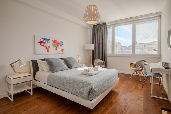A modern bedroom with a bed, bedside table, lamp, and a desk with a chair.