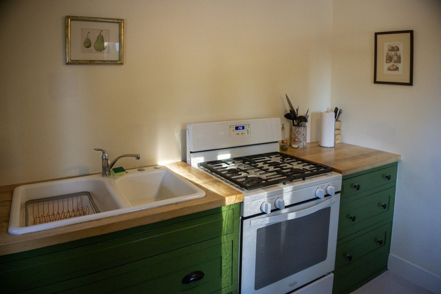 A compact kitchen with a sink, stove, and green cabinetry.