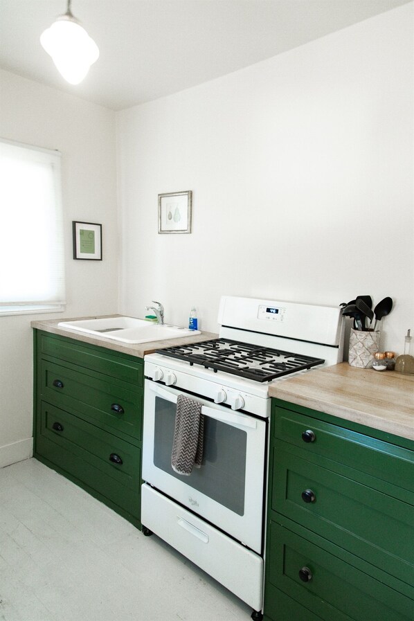 A kitchen with a white stove, green cabinets, a sink, and a window.