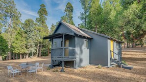A small cabin with a porch, a table with chairs, and a staircase leading to a door.