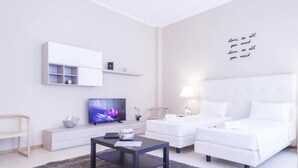 Une chambre d’hôtel moderne équipée d’un téléviseur à écran plat, de deux lits blancs, d’une petite table et d’un mur orné d’une citation inspirante.