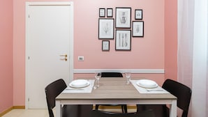 Un coin repas avec une table dressée pour deux personnes, des œuvres d’art encadrées au mur et une porte blanche.