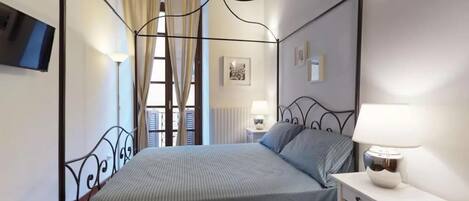 A four-poster bed with a striped bedspread, a bedside table with a lamp, and a window with curtains.