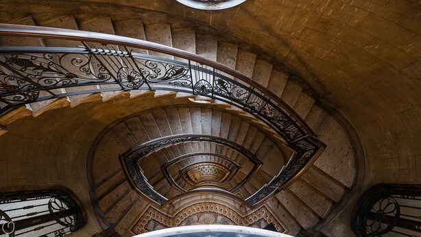Un escalier en colimaçon orné de rampes en métal ouvragé et de marches en pierre.