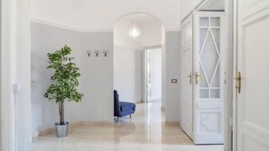 Un couloir avec une plante en pot, une chaise bleue et une porte blanche ornée d’un motif géométrique.