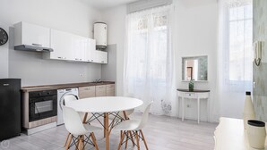 A modern kitchen with white cabinetry, a built-in oven, and a dining area with a white table and chairs. - Italianway - Montello 10 - C (Milan)