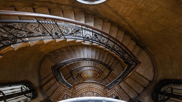 A spiral staircase with ornate metal railings and a stone wall. - Italianway - Montello 10 - C (Milan)