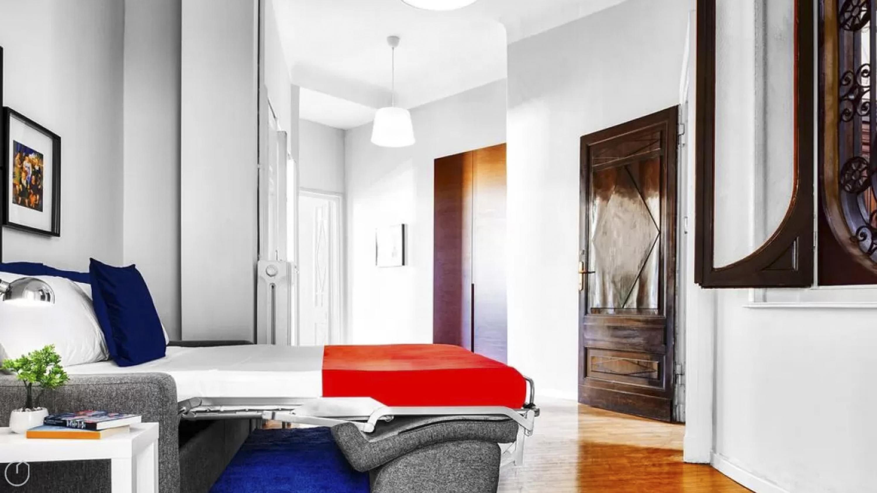 A modern hotel room with a bed, a desk, and a chair. There is a window with a view of the outside.