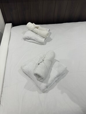 A neatly made bed with white linens and two rolled towels placed on it. - Studio Sleeps 2 - Paid On-Street Parking (London)