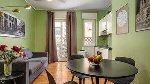 A cozy living room with a sofa, a dining table with fruit, a kitchen area, and a balcony with curtains. - Italianway - Bartolini 9 - Piccolo (Milan)