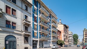 A multi-story building with balconies, a garage door, and a clear blue sky. - Italianway - Bartolini 9 - Piccolo (Milan)