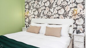 A neatly made bed with two pillows, a green throw blanket, and a floral wallpaper pattern on the wall. - Italianway - Bartolini 9 - Piccolo (Milan)