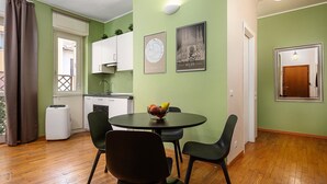 A compact living space with a kitchenette, a dining area with a round table and chairs, and a small window with curtains. - Italianway - Bartolini 9 - Piccolo (Milan)