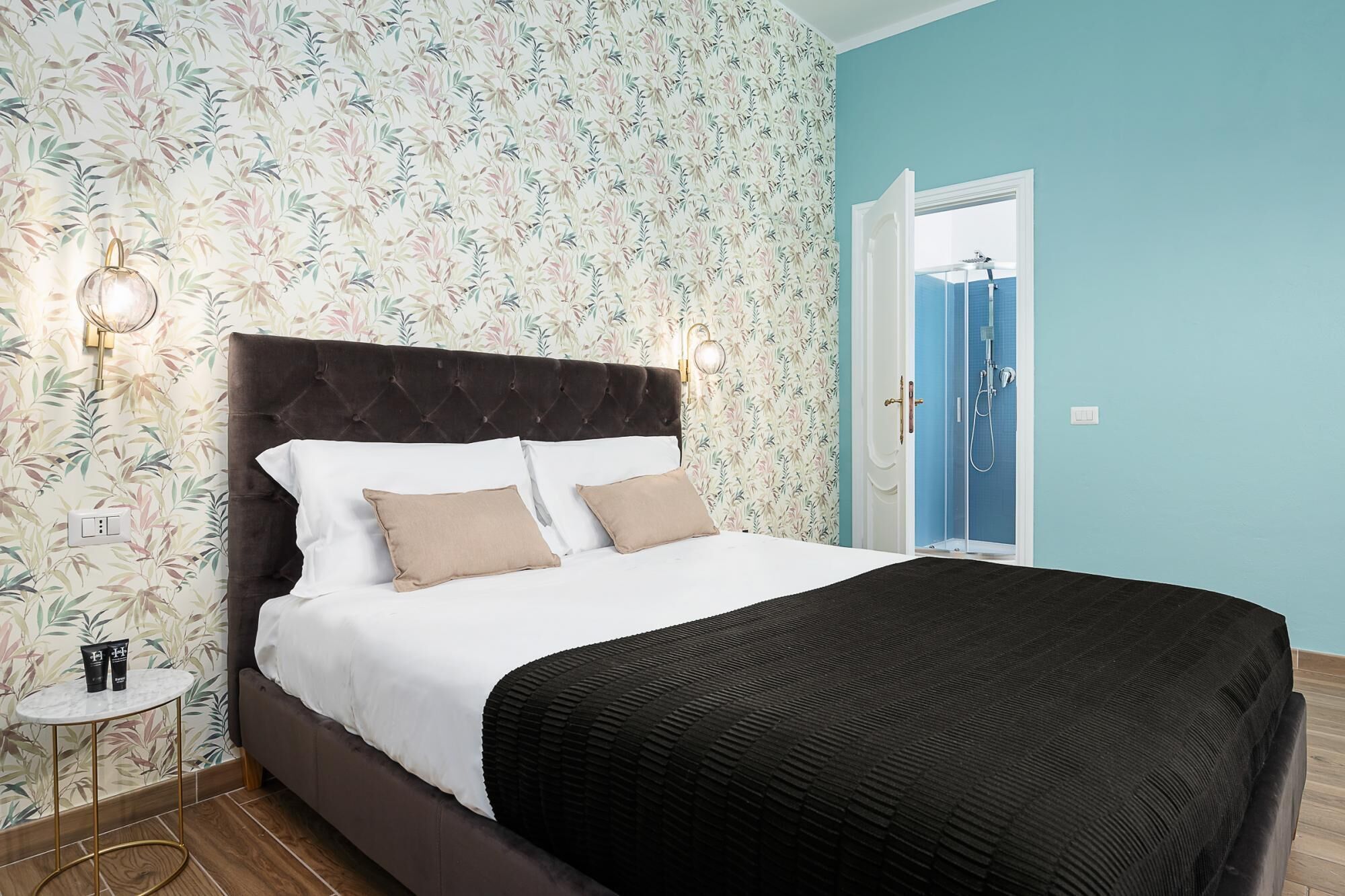 Une chambre à coucher avec un lit, deux lampes fixées au mur, une porte donnant sur une salle de bain et une petite table sur laquelle se trouvent divers objets.
