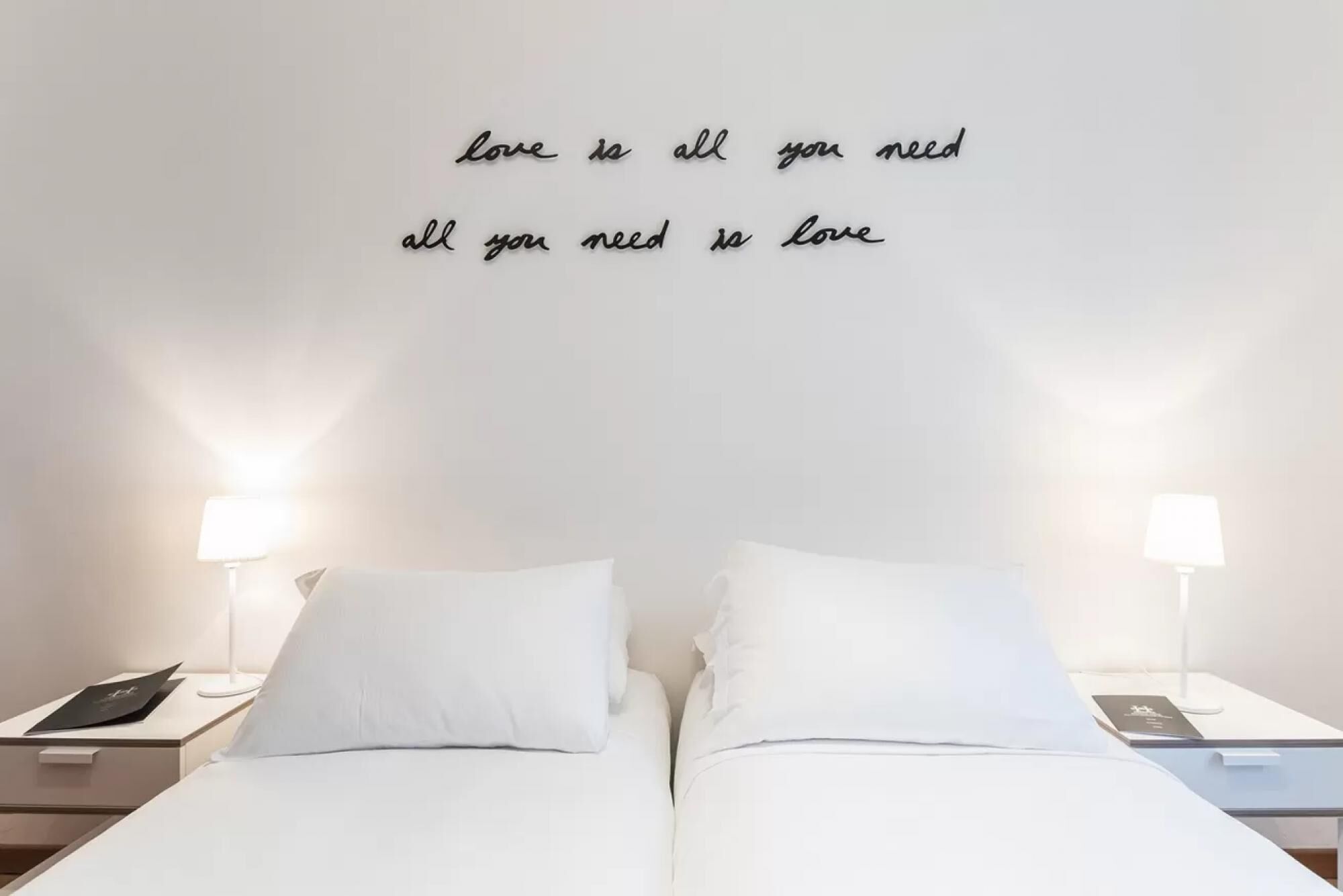 Una camera d'albergo con un letto, due comodini e una parete con una citazione motivazionale.