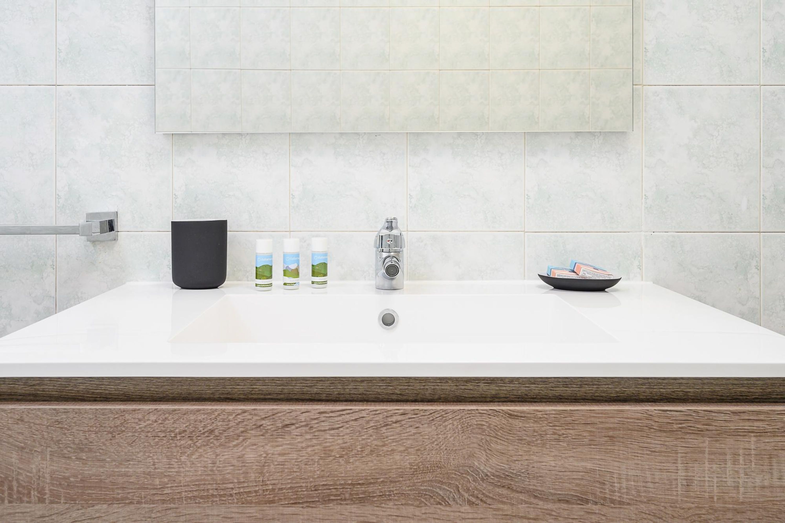 A modern bathroom with a large bathtub, a black soap dispenser, three bottles of liquid soap, a silver faucet, and a small bowl with items on the edge of the tub.