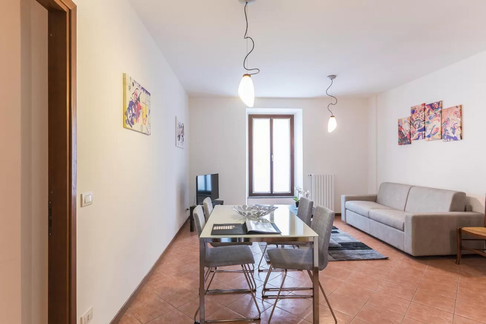A modern living room with a sofa, a dining table with chairs, and a TV.
