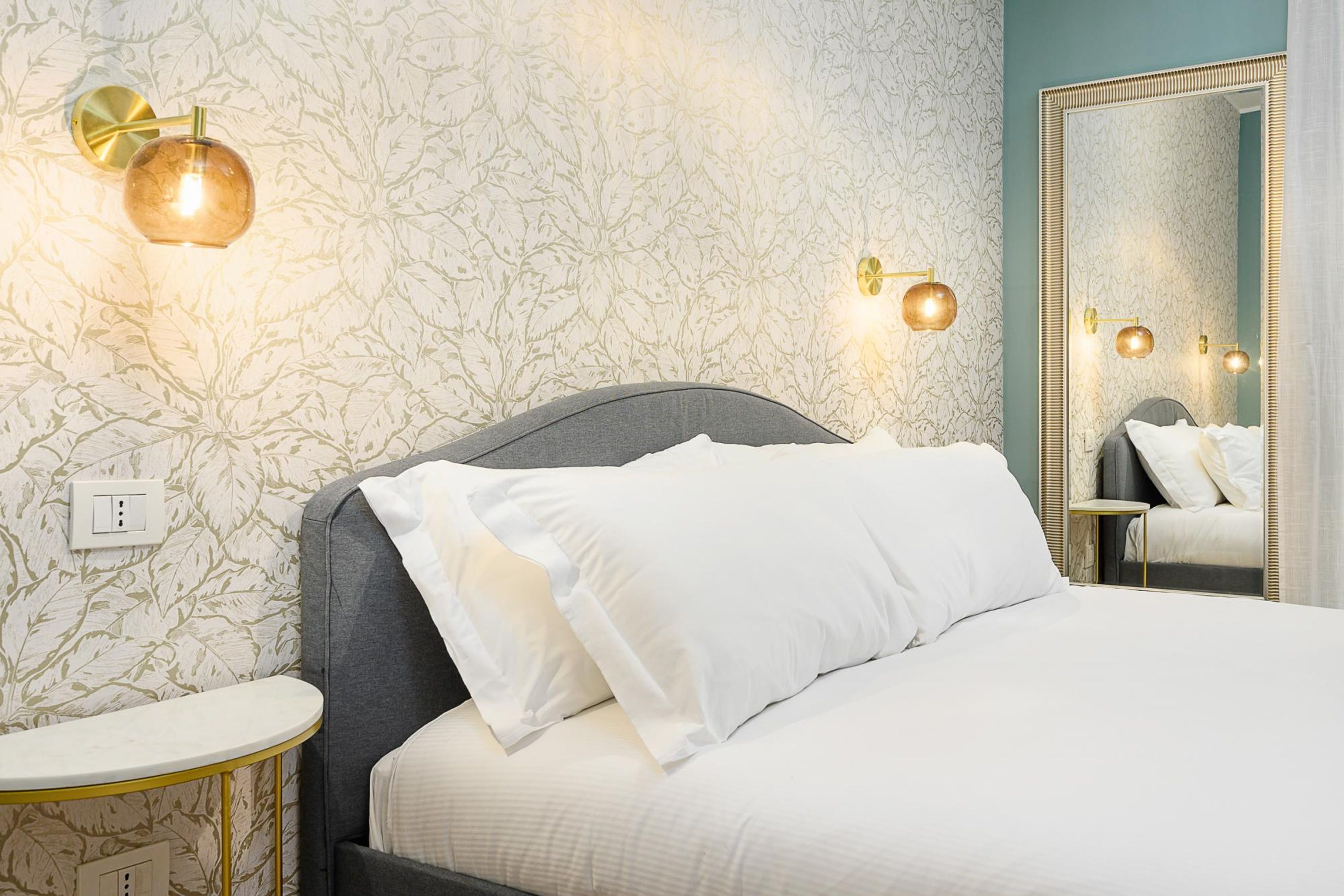 Un dormitorio con una cama, una mesita de noche, un espejo y apliques en la pared.