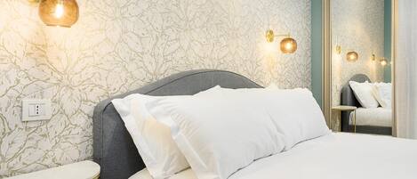 Un dormitorio con una cama, una mesita de noche, un espejo y apliques en la pared.