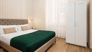 Une chambre à coucher comprenant un lit, une table de chevet, une lampe, une armoire et des rideaux légers.