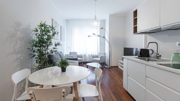 Eine moderne Küche mit weißen Schränken, eine Essecke mit rundem Tisch und Stühlen sowie ein großes Fenster mit durchscheinenden Vorhängen.