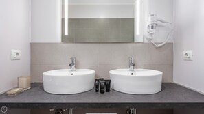 Ein Badezimmer mit zwei weißen Waschbecken, einem Spiegel und einem an der Wand montierten Föhn.