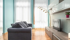 A modern living room with a grey sofa, a flat-screen TV on a wooden cabinet, and a floor lamp. - Italianway Collection - Cannobio 8 - Norma (Milan)
