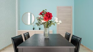 A dining area with a rectangular table, six chairs, a vase with flowers, a round mirror, and a light blue wall. - Italianway Collection - Cannobio 8 - Norma (Milan)