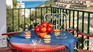 A table with a bowl of apples and pastries on a balcony overlooking a coastal view.