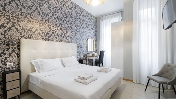 Habitación de hotel con una cama grande, un escritorio con silla, un espejo y un televisor montado en la pared.