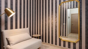 Una habitación con papel tapiz a rayas, un espejo grande con marco dorado, un sofá y una pequeña mesa redonda.