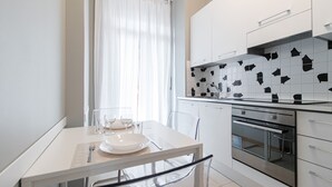 Una cocina moderna con armarios blancos, un salpicadero de azulejos blanco y negro, electrodomésticos de acero inoxidable y un comedor con mesa y sillas blancas.