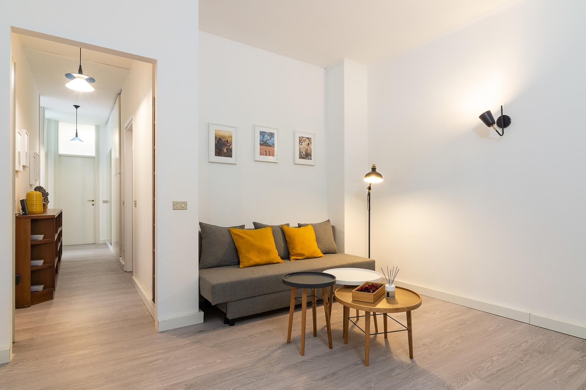 Un salón moderno con un sofá gris, cojines amarillos, una pequeña mesa redonda con una vela y una lámpara de pie.