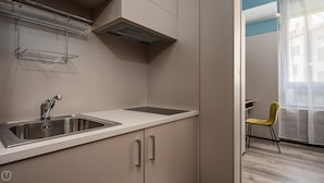 Una cocina moderna con un lavamanos de acero inoxidable, horno empotrado y una ventana con cortinas de gasa.