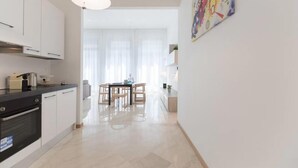 Una cocina moderna con armarios blancos, encimera negra y comedor con sillas y mesa de madera.