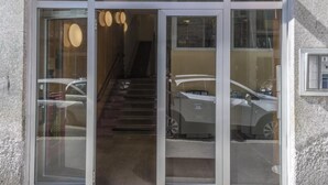 Una entrada de hotel con puerta de cristal, una escalera que conduce al interior y un estacionamiento visible a través del cristal.