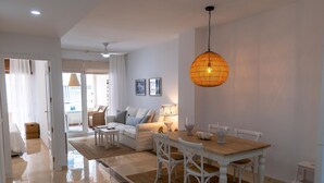 A spacious living room with a white sofa, a dining table, and a hanging light fixture. - Suitur Milenium apartment Marbella beach Venus (MARBELLA)