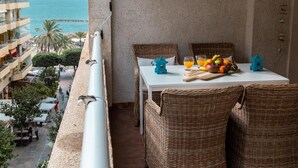 A balcony with wicker furniture, a table with fruit, and a view of the ocean and buildings. - Suitur Milenium apartment Marbella beach Venus (MARBELLA)