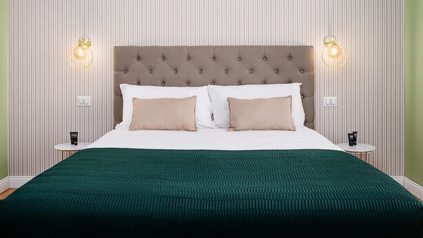 Un letto rifatto con cura, una coperta verde, due comodini con lampade e una carta da parati a righe.