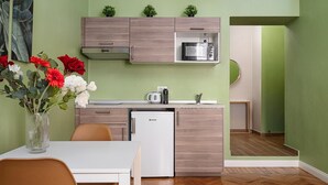 Una cucina compatta con forno a microonde, macchina del caffè e piccolo frigorifero. C'è un tavolo da pranzo con sedie e un vaso di fiori.