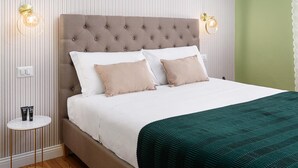 Un letto con testiera trapuntata, biancheria bianca e due cuscini color beige. Due applique sono posizionate su ciascun lato del letto.