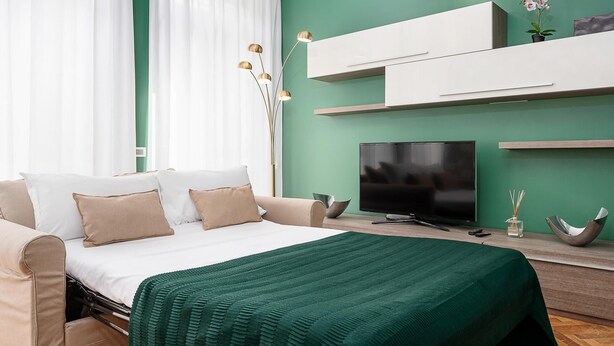 Een moderne slaapkamer met een bed, een televisie en een groene wand.